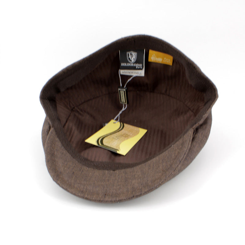 A brown wool flat cap with a ribbed brown corduroy interior, shown from a top-down view on a white background. A black and white brand tag and a yellow paper tag are attached to the interior.