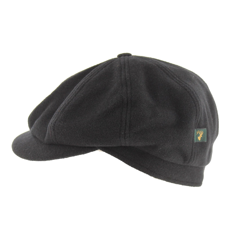 A black wool flat cap with a small green and gold embroidered logo patch on the side, shown against a plain white background.