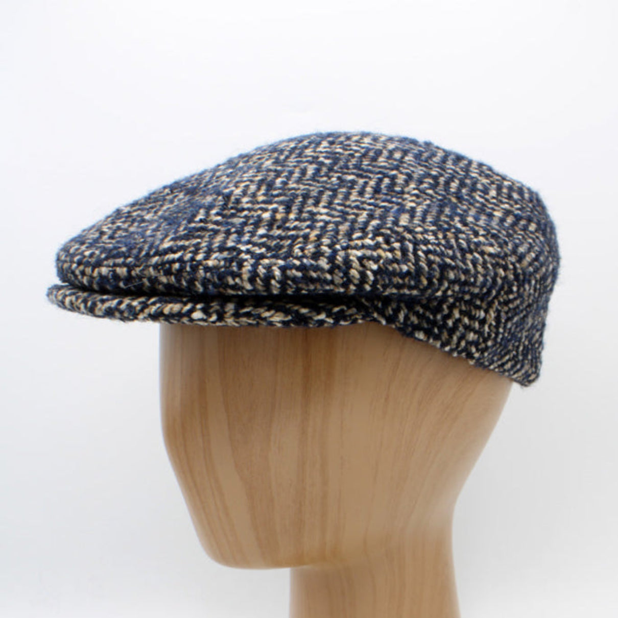 Herringbone patterned cap on a wooden mannequin head against a white background