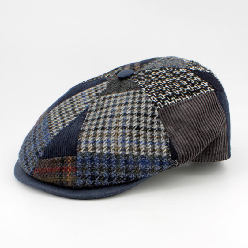 A patchwork flat cap made of multiple textured fabrics including houndstooth, corduroy, and tweed in shades of navy, gray, brown, and black, photographed on a seamless white background.