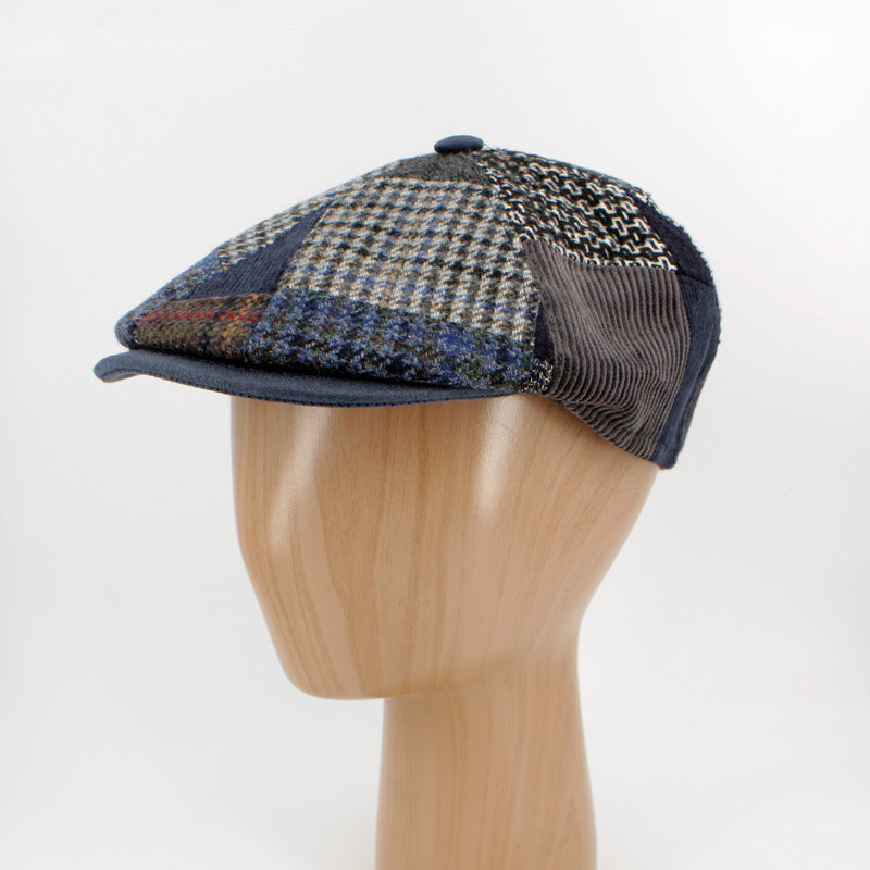 A vintage-style flat cap with a blue, beige, and brown houndstooth patterned front panel and a dark navy mesh back, displayed on a wooden mannequin head against a white background.