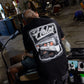 A man wearing a black graphic t-shirt with a large white and gray 'Halo' car design on the back, seen from behind while working at a barber station in a shop.