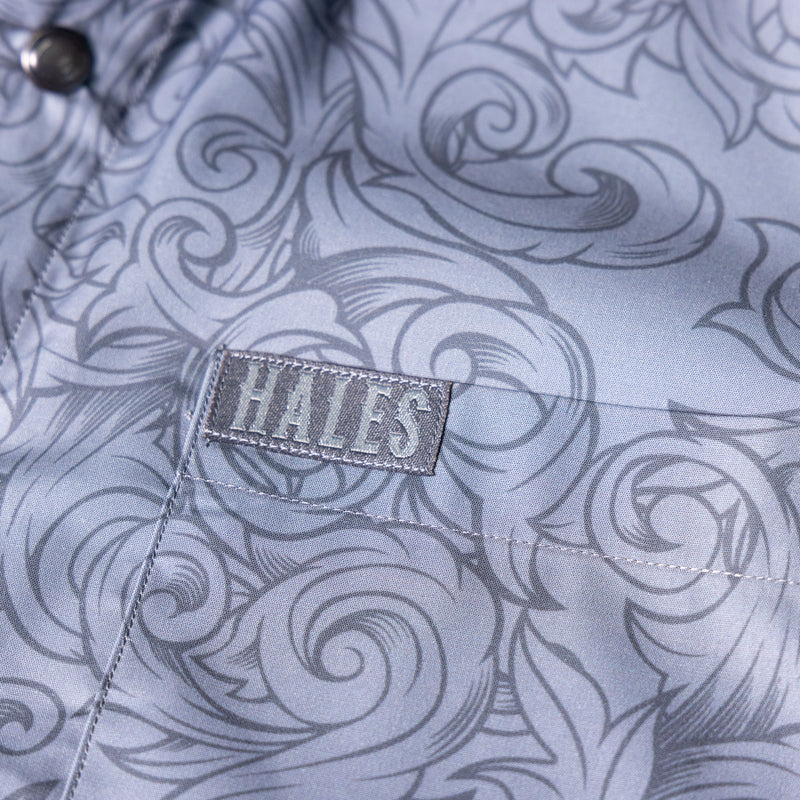 Close-up of a light blue-gray patterned shirt pocket with a gray embroidered Hales brand patch.