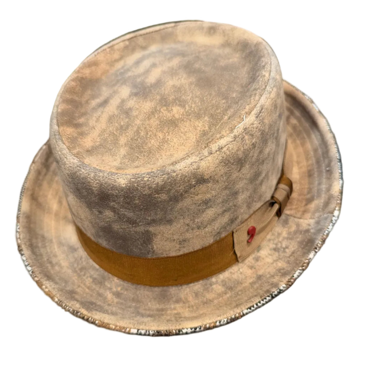A vintage-style felt hat with a distressed beige and brown finish, featuring a tan band with a small red heart detail, resting on a white surface.