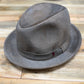 A distressed gray felt fedora hat with a matching band and a small red accent, resting on a rustic wooden plank surface.
