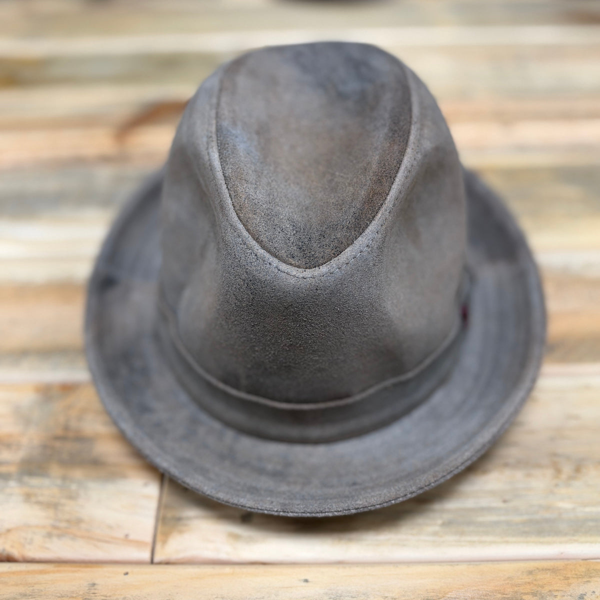 A distressed gray felt fedora hat resting on a rustic wooden plank surface.