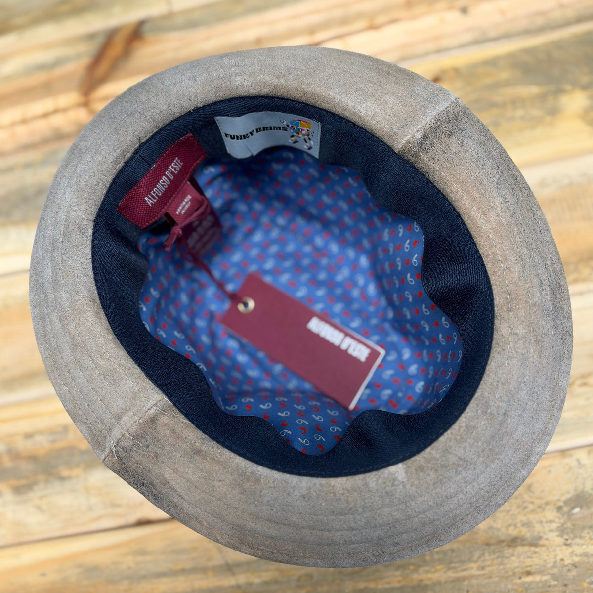 A top-down view of a gray felt hat with a navy blue inner band and a blue patterned interior lining.