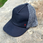 A baseball cap with a dark navy leather front and bill, and a textured gray fuzzy mesh back, resting on a stone surface.