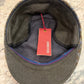 An overhead view of a wool cap's interior, showing a dark olive green wool body, a gray inner lining, and a red hanging tag.