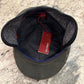 An olive green wool cap with a black felt underbrim and a red interior tag, photographed from above on a speckled granite countertop.
