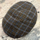 A classic flat cap made of brown and blue tweed with a subtle plaid pattern, resting on a speckled granite countertop.