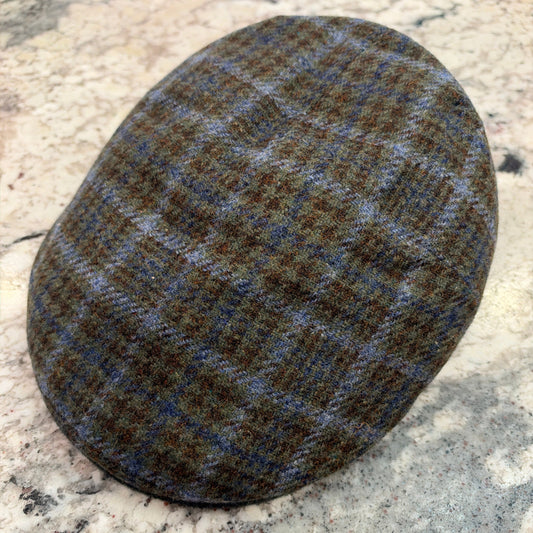 A classic flat cap made of brown and blue tweed with a subtle plaid pattern, resting on a speckled granite countertop.
