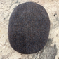 A classic flat cap in a dark brown and gray herringbone tweed pattern, resting on a light-colored stone surface.