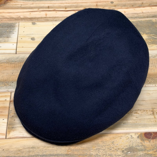 A dark navy blue wool flat cap resting on a rustic wooden plank surface.