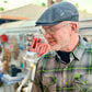 A man wearing a gray flat cap, wire-rimmed glasses, and a gray plaid short-sleeve button-up shirt with neon green lines and buttons. The shirt has a small green 'HALES' brand tag on the chest pocket.