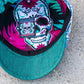 Close-up of a baseball cap with a teal green visor and a colorful printed inner crown featuring a large sugar skull design and floral patterns.