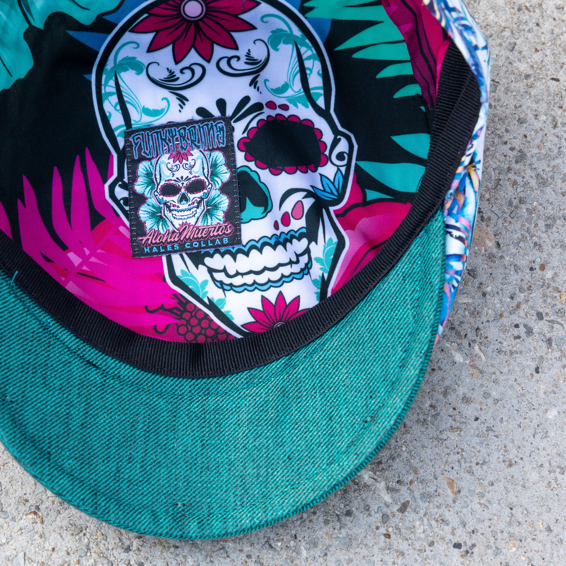 Close-up of a baseball cap with a teal green visor and a colorful printed inner crown featuring a large sugar skull design and floral patterns.