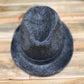 A dark gray textured fedora hat with a wide brim, photographed from a top-down perspective on a light brown wooden surface.