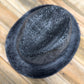 A black felt fedora hat with a textured, speckled finish, photographed from a top-down angle on a light-colored wooden plank surface.