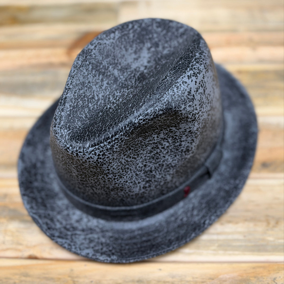 A black and gray speckled fedora hat with a black band, photographed from a top-down angle on a light wood background.