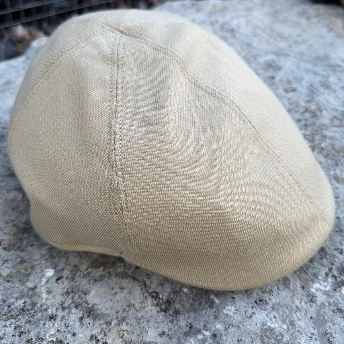 A beige canvas flat cap resting on a textured gray stone surface.