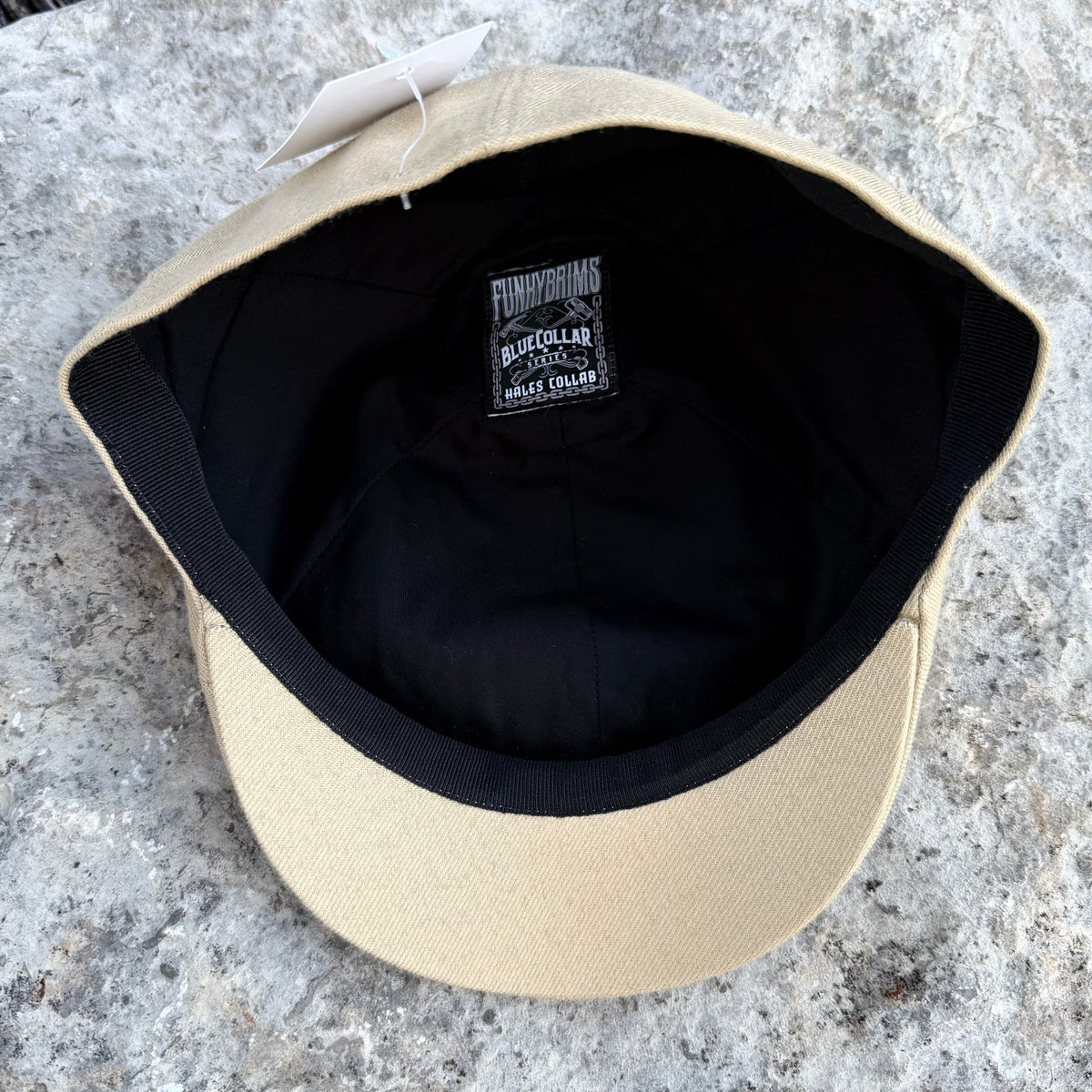 A beige baseball cap viewed from above, showing a black interior lining and a small black brand patch that reads 'Buckeye Park'.