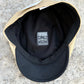 A close-up top-down view of a baseball cap with a tan crown and black visor, showing the black interior lining and a central sewn label that reads 'FLYING BRIMS BLUE COLLAR'.