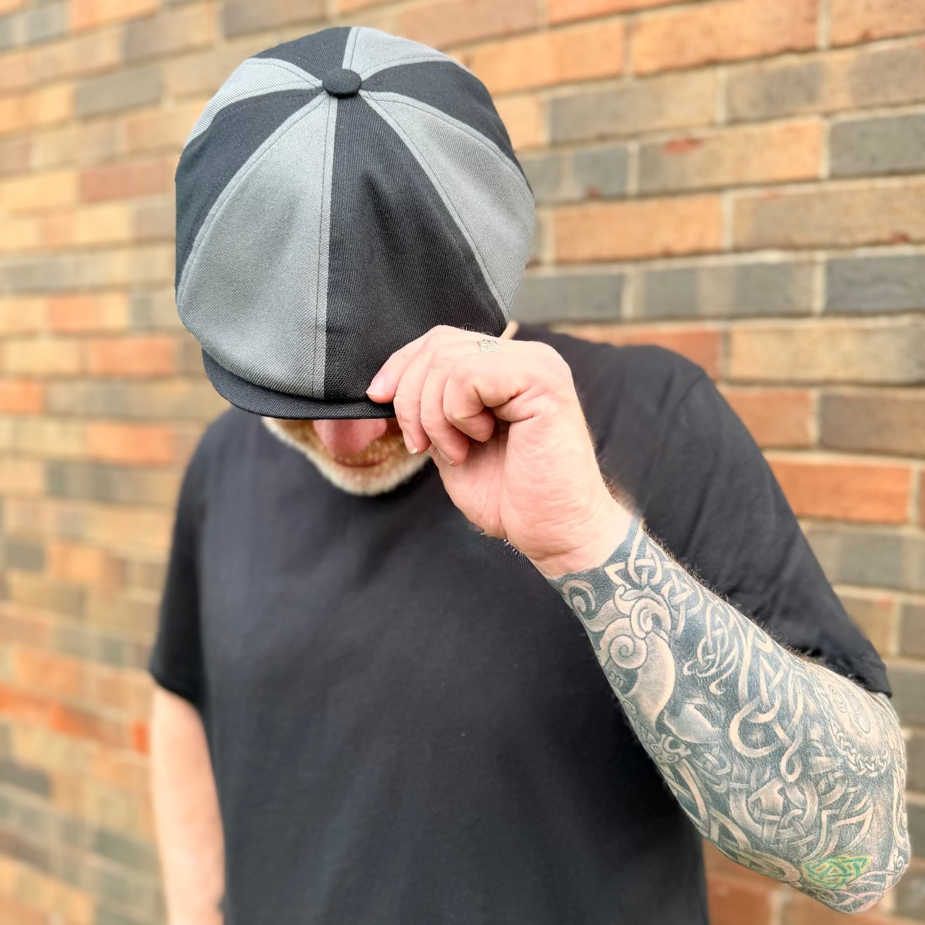 Person wearing a gray and black cap with a brick wall background