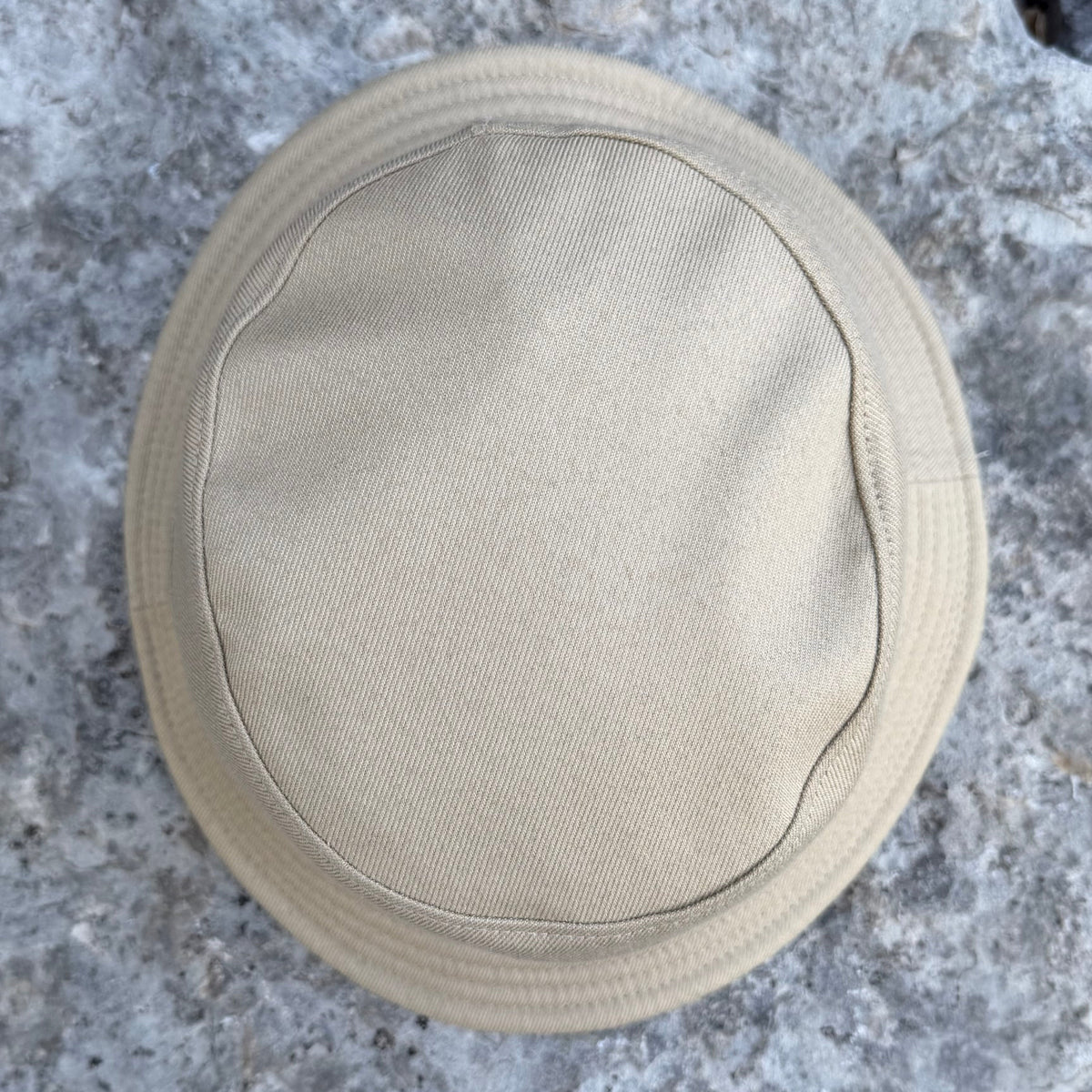 A beige fabric hat or cap laid flat on a gray stone surface, photographed from above.