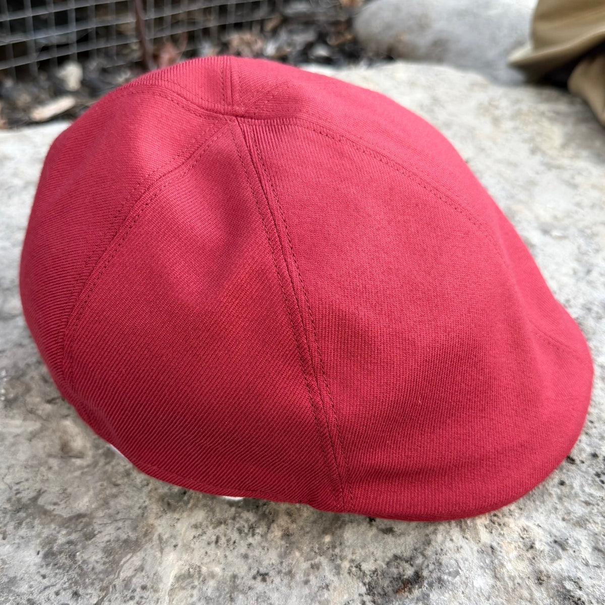 A red flat cap made of textured canvas fabric, resting on a gray stone outdoors.