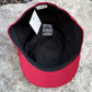 A red and black baseball cap shown from the inside, resting on a gray stone surface. The cap features a red crown and brim, a black interior, a black ribbed trim, a white hangtag, and a black interior label reading 'Blue Collar Caps'.