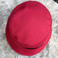 A red bucket hat with a black band, photographed from a top-down angle on a textured gray stone surface.