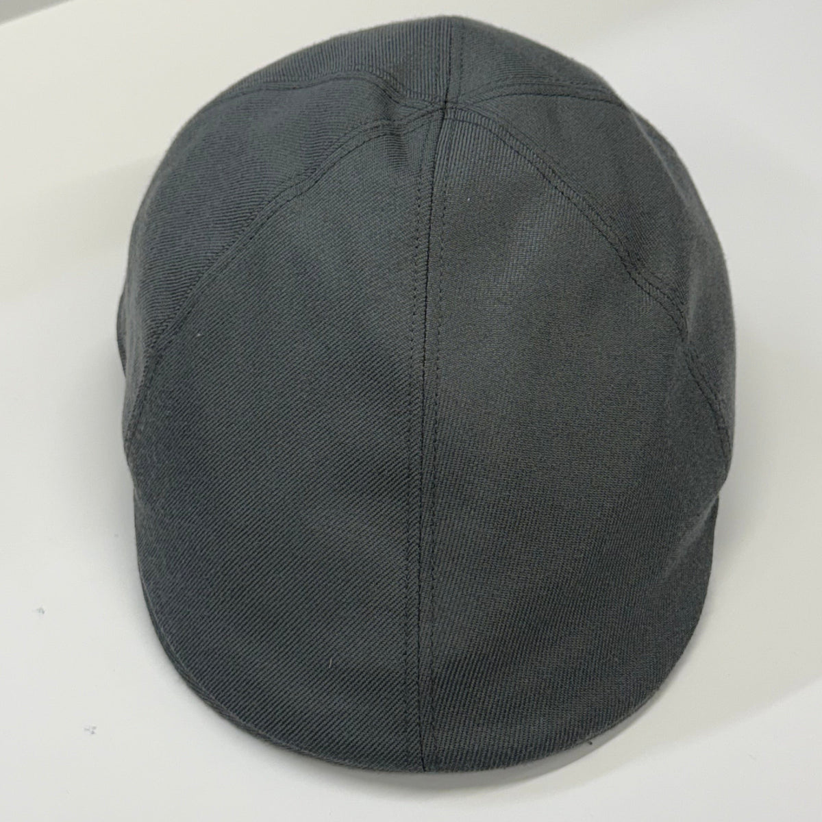 A dark gray fabric flat cap with a curved brim, photographed from a top-down angle on a plain white surface.