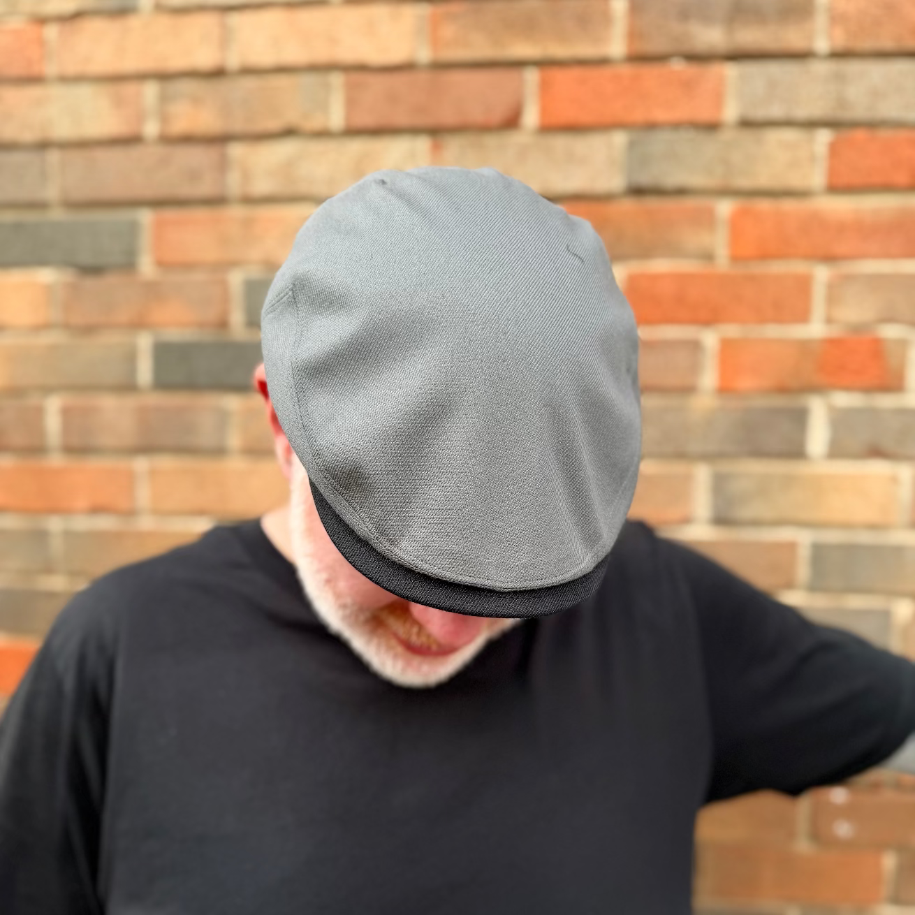 Person wearing a gray cap and black shirt against a brick wall.