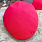 A close-up of a bright red fabric cap with a gray ribbed trim, resting on a textured stone surface.