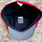 A red and gray baseball cap viewed from the inside, showing a black interior lining with a central sewn label that reads 'FUNKYBRIMS BLUE COLLAR 100% HALES COLLAB'. The cap is photographed on a textured stone surface.