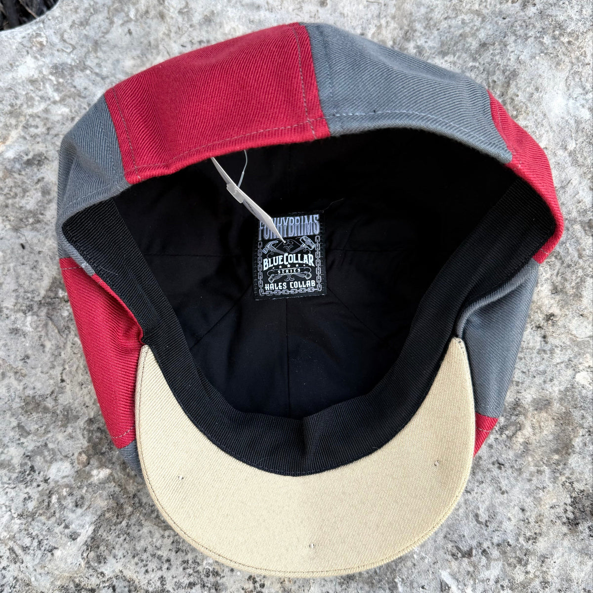 A vintage-style baseball cap with red, gray, and beige panels, photographed from the inside. The brand label 'Blue Collar' is visible inside the crown.