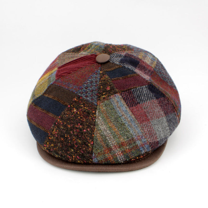 A multicolor patchwork plaid flat cap hat with a brown leather visor and a brown button on top, photographed on a clean white background.