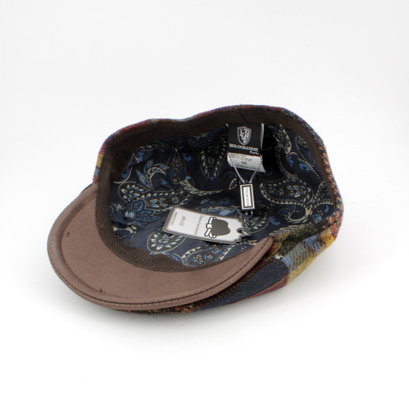 A vintage-style flat cap shown from an overhead angle on a white background, featuring a brown leather visor and a dark blue paisley patterned fabric crown.