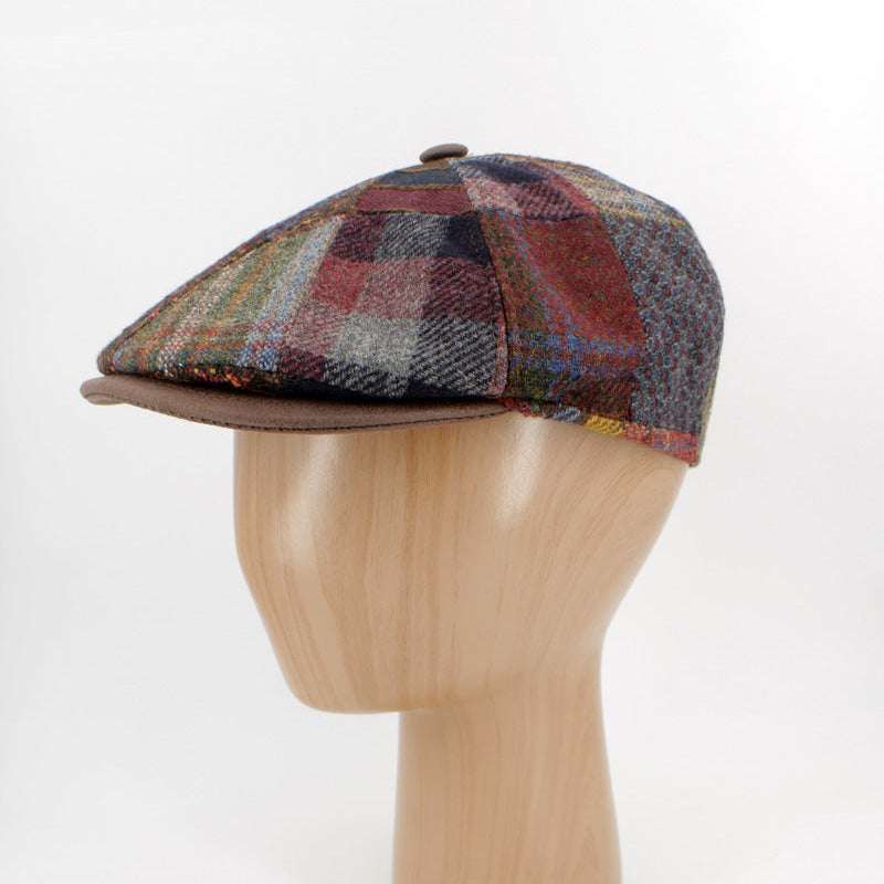 A vintage-style plaid flat cap with a brown visor, displayed on a light wood mannequin head against a white background.