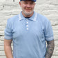 Man wearing a light blue polo shirt and cap standing against a light stone wall.