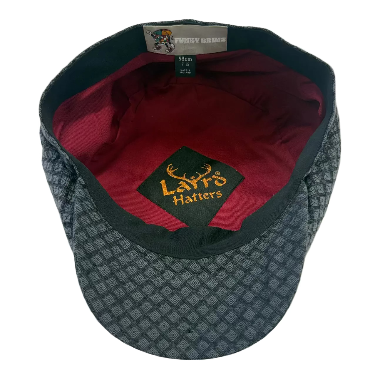 A vintage patterned flat cap with a dark gray and black geometric design, a dark green interior band, and a burgundy red inner lining. The front crown features a black patch with gold embroidered 'Laffy Hatters' logo and deer antlers.