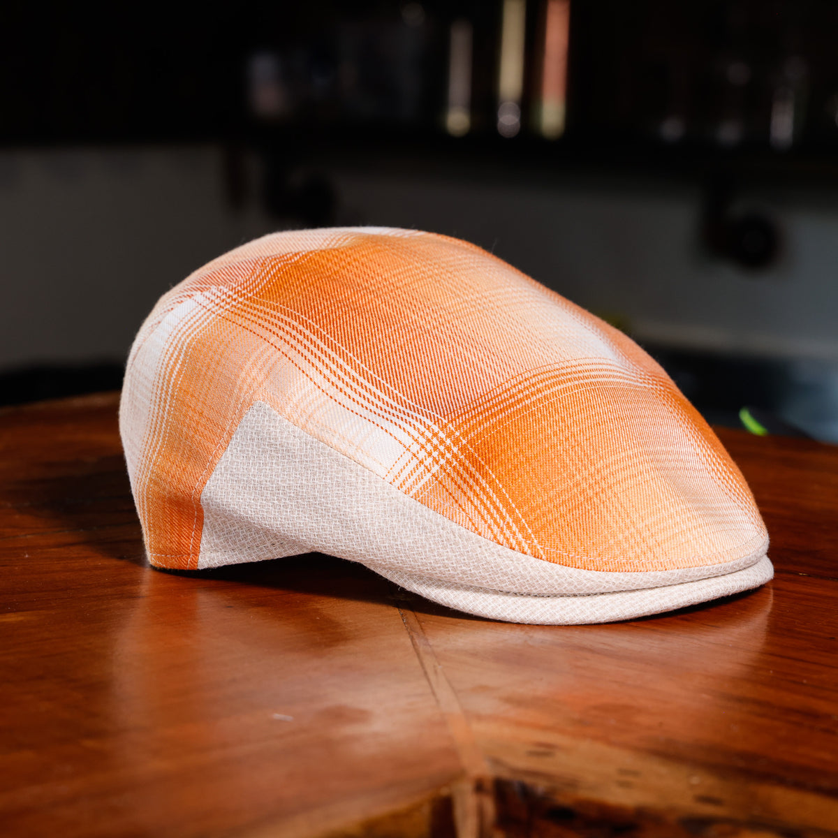 An orange and white plaid flat cap resting on a polished wooden table.