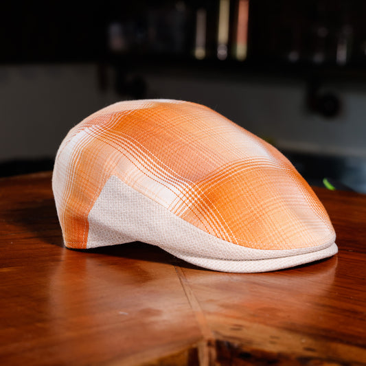 An orange and white plaid flat cap resting on a polished wooden table.