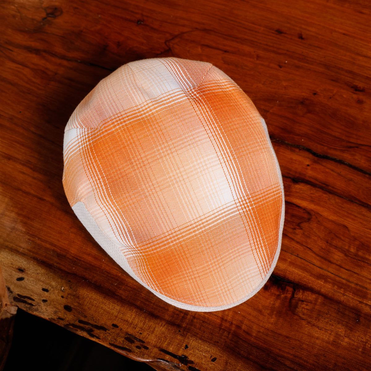 A low-cut cap with an orange and white plaid pattern, resting on a rustic wooden surface.