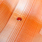 Close-up of an orange and white plaid fabric with a single red oval button on a button placket.