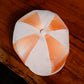 A structured flat cap with alternating white and orange plaid panels, photographed from directly above on a rustic wooden table.