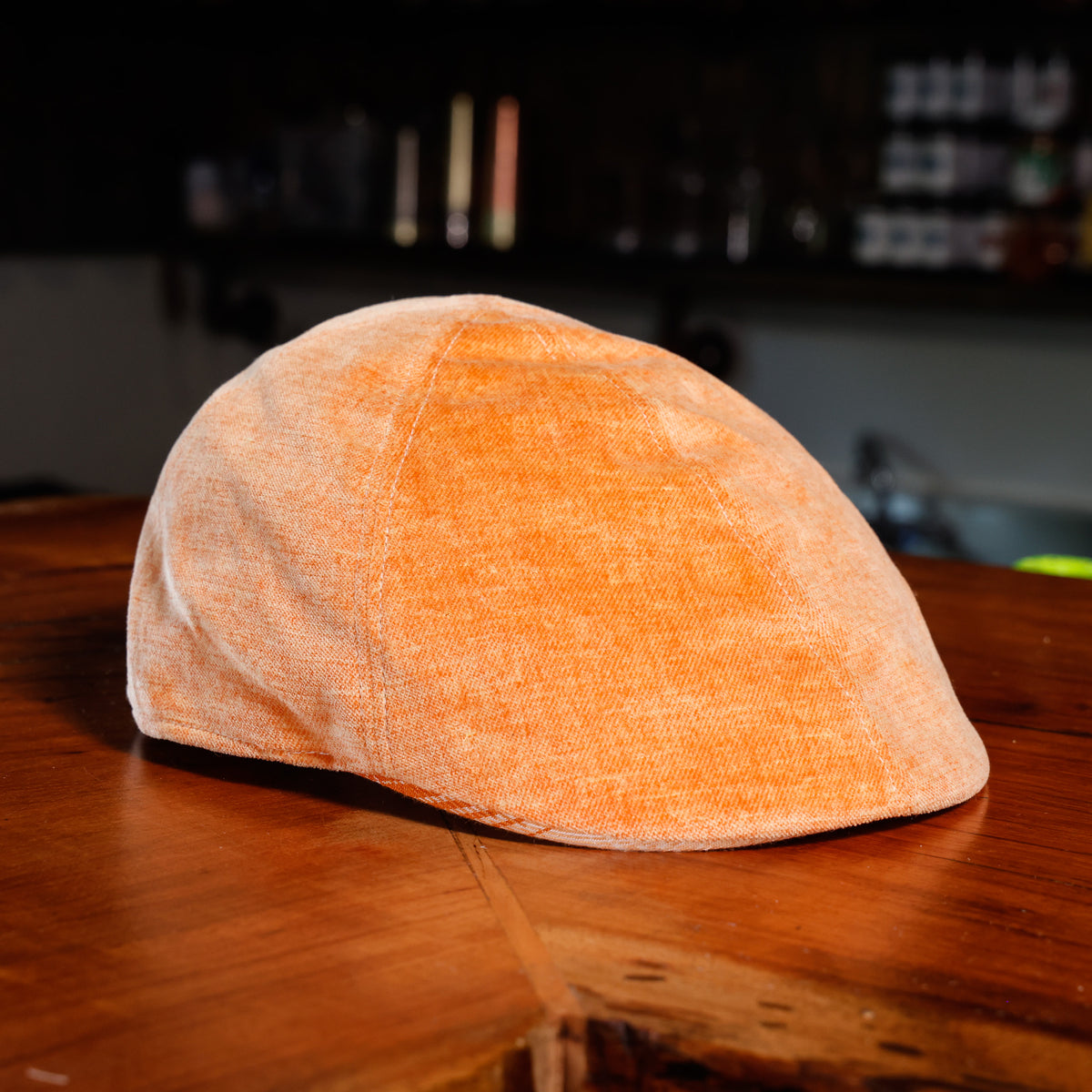 An orange textured flat cap resting on a wooden table with a dark, blurred background.