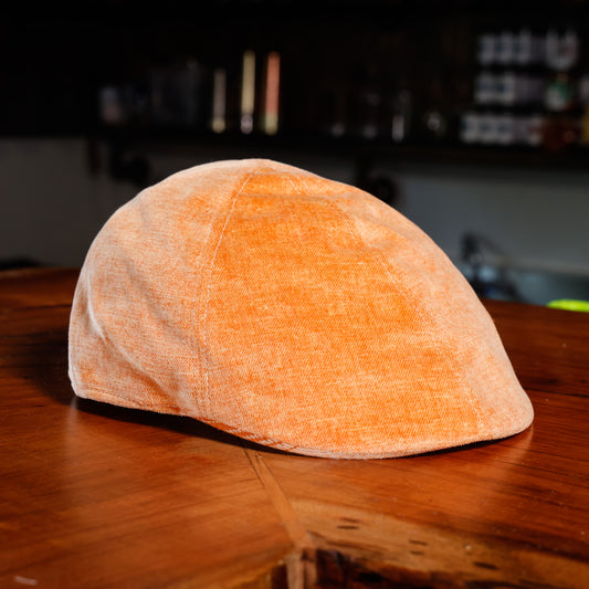 An orange textured flat cap resting on a wooden table with a dark, blurred background.