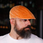 A man with a full beard wearing a textured orange flat cap, photographed in a dimly lit bar setting.